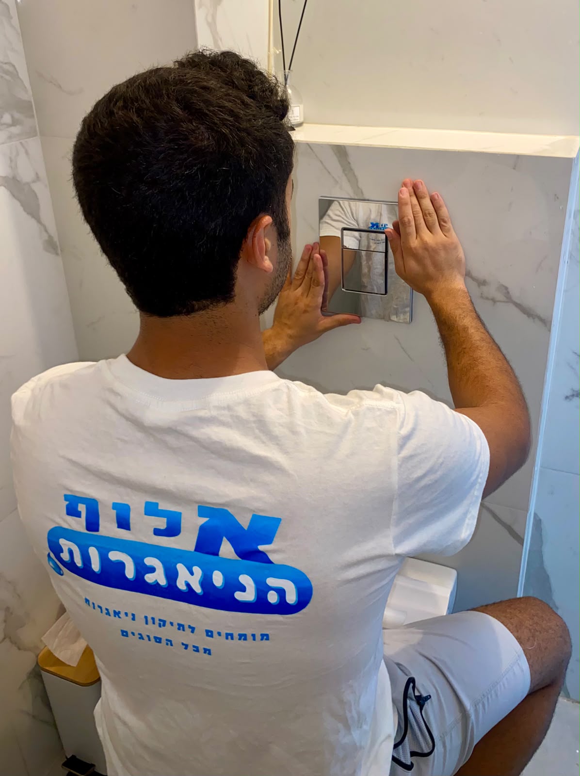 טכנאי אלוף הניאגרות מתקין לחצן הדחה סמוי
